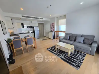 Spacious modern living room with open kitchen and dining area, featuring stylish furniture and wooden flooring.