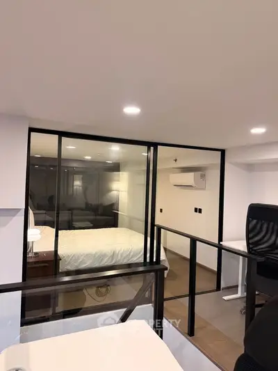 Modern loft bedroom with glass partition and office space, featuring sleek design and cozy ambiance.