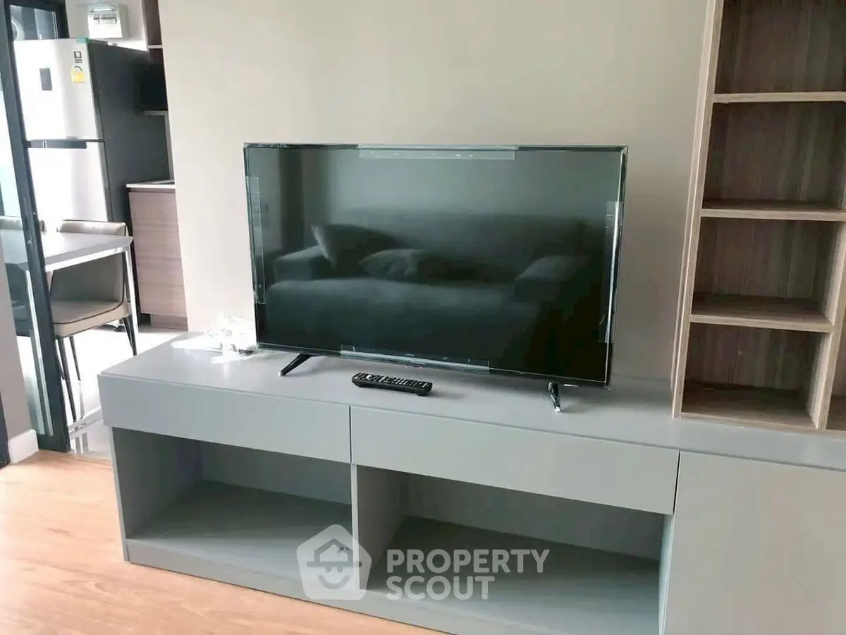 Modern living room with sleek TV stand and flat-screen TV, adjacent to a stylish kitchen area.