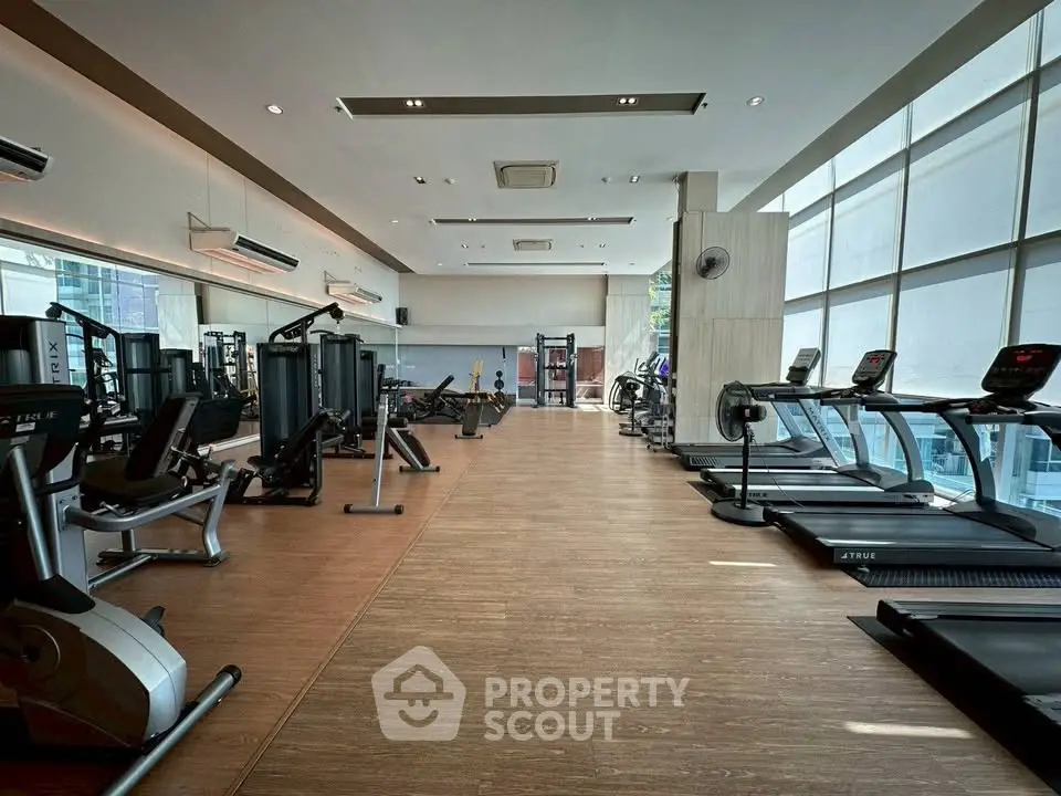 Spacious modern gym with state-of-the-art equipment and large windows for natural light.