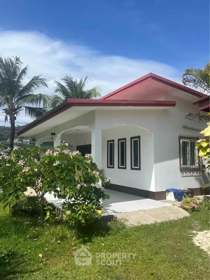 Charming tropical home with lush garden and palm trees under a clear blue sky.