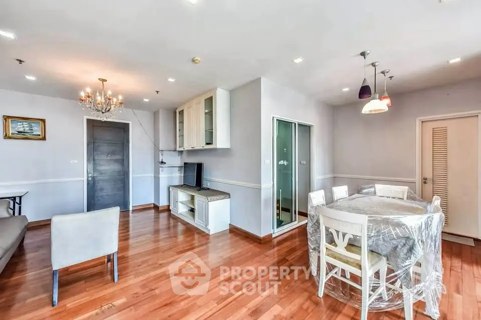 Spacious living room with elegant chandelier and hardwood floors in modern apartment.