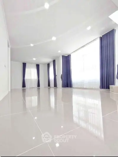 Spacious modern living room with glossy tile flooring and large windows with elegant curtains.