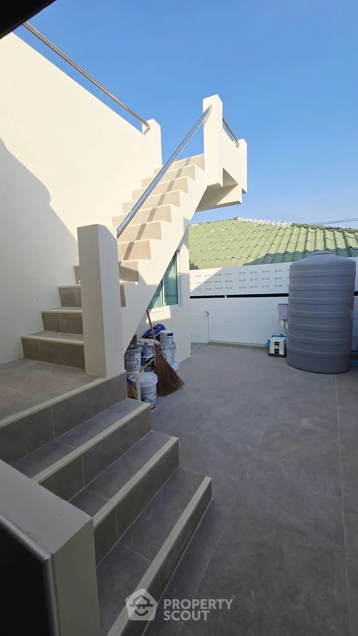 Modern rooftop terrace with stairs and storage tank under clear blue sky.