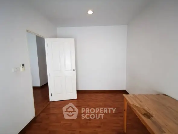 Minimalist room with wooden floor and table, white walls, and open door.