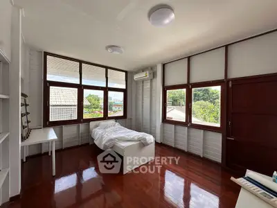 Bright and airy bedroom with wooden floors and large windows offering lush garden views.