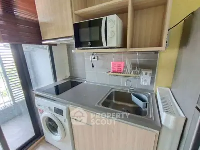 Compact modern kitchen with washing machine and microwave, ideal for urban living.