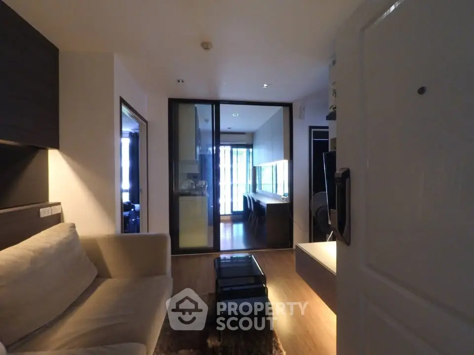 Modern living room with cozy sofa and glass partition leading to a stylish kitchen.