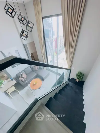 Modern duplex interior with stylish staircase and large windows offering city views.