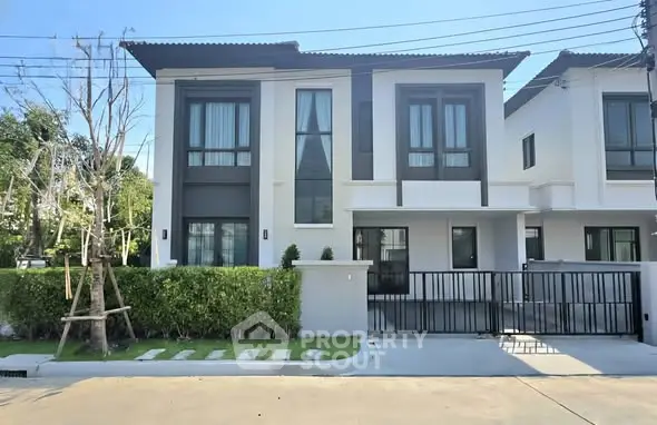 Modern two-story house with sleek design and gated entrance in a suburban neighborhood.