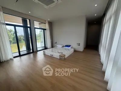 Spacious bedroom with large windows and scenic view, featuring minimalist decor and wooden flooring.
