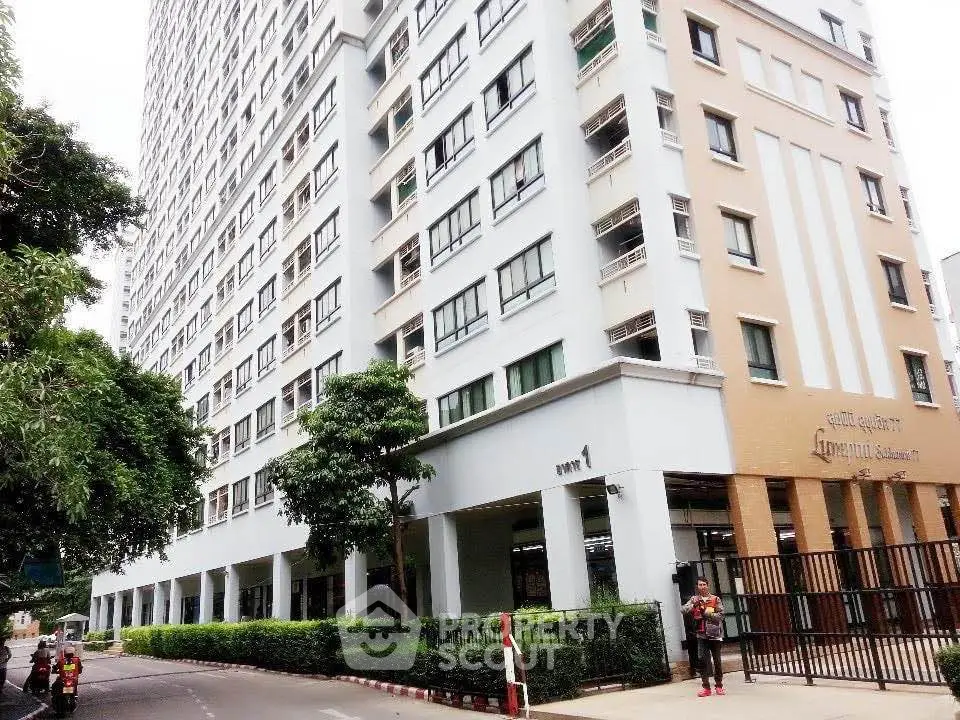 Modern high-rise building exterior with lush greenery and secure entrance in urban setting.