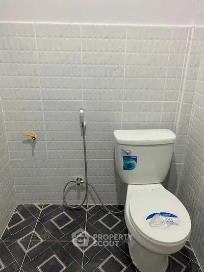 Modern bathroom with tiled walls and floor featuring a toilet and bidet spray.