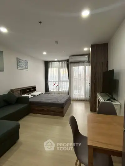 Modern studio apartment with cozy bed, sofa, and dining area, featuring large windows and stylish decor.