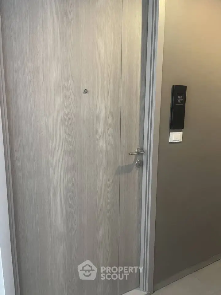 Modern apartment entrance with sleek wooden door and digital room number display.