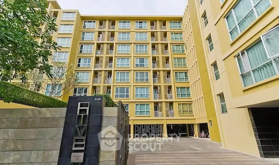 Modern yellow apartment building with spacious courtyard and lush greenery.