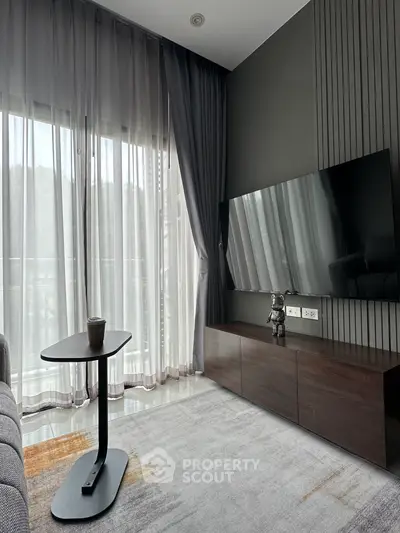 Modern living room with sleek TV setup and large windows offering natural light.