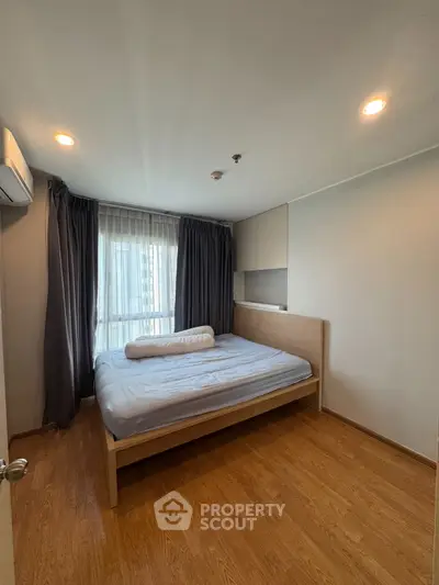 Cozy bedroom with wooden flooring and natural light from large window.