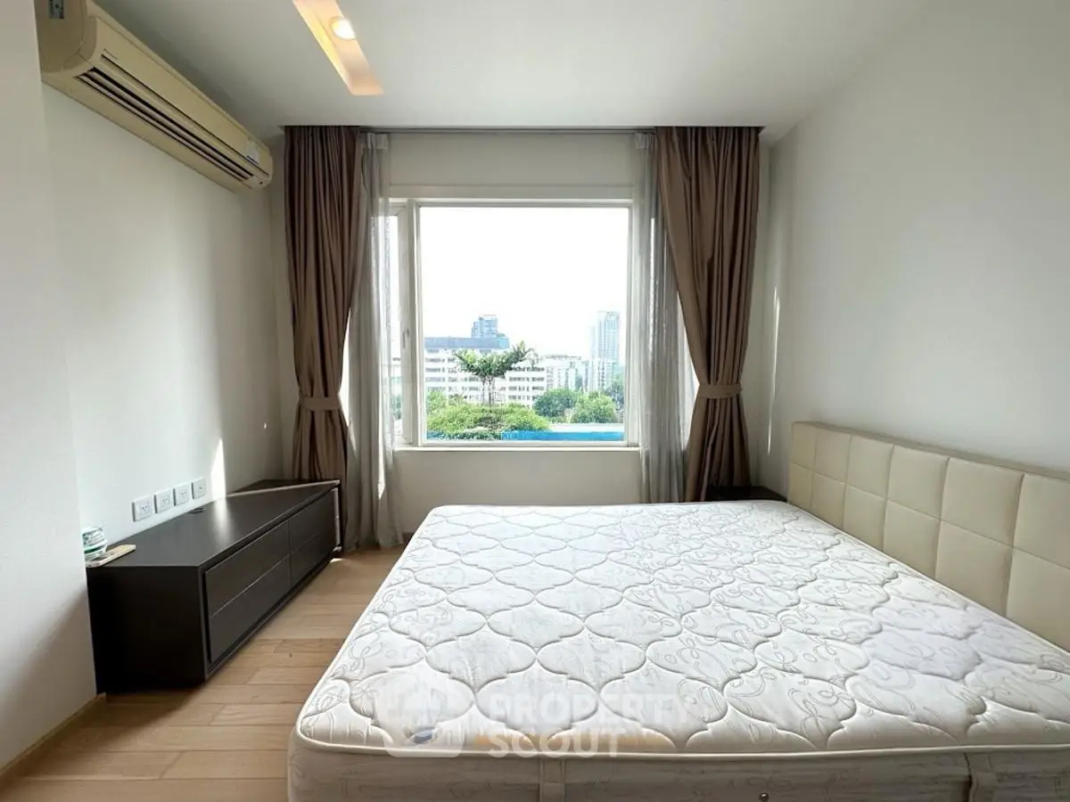 Spacious bedroom with large window offering city views, featuring modern furnishings and natural light.