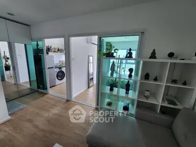 Modern living room with stylish decor and glass shelving, featuring a view into a sleek kitchen with appliances.