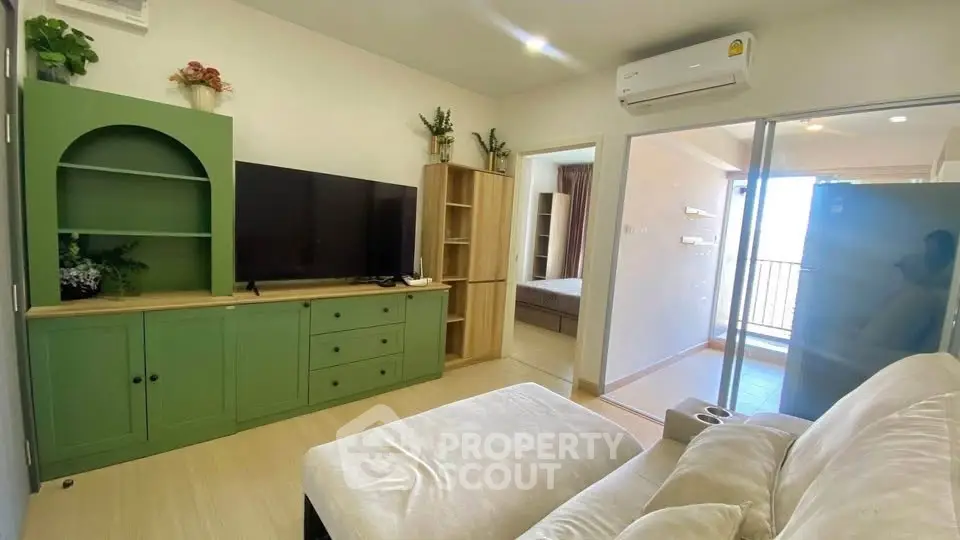 Modern living room with green cabinetry and cozy sofa, leading to a bright bedroom with balcony access.