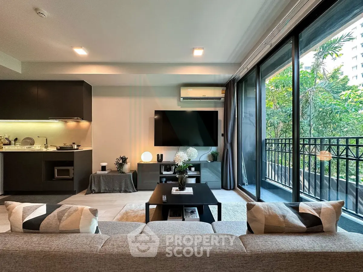 Modern living room with open kitchen and large balcony, featuring sleek design and abundant natural light.