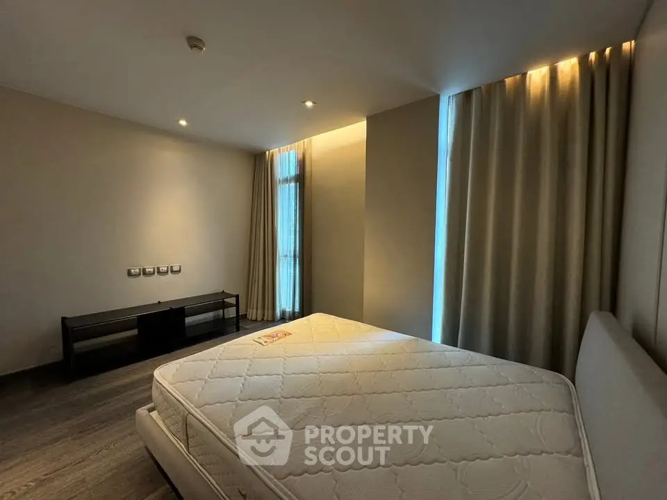Spacious bedroom with modern lighting and large windows in a contemporary apartment.