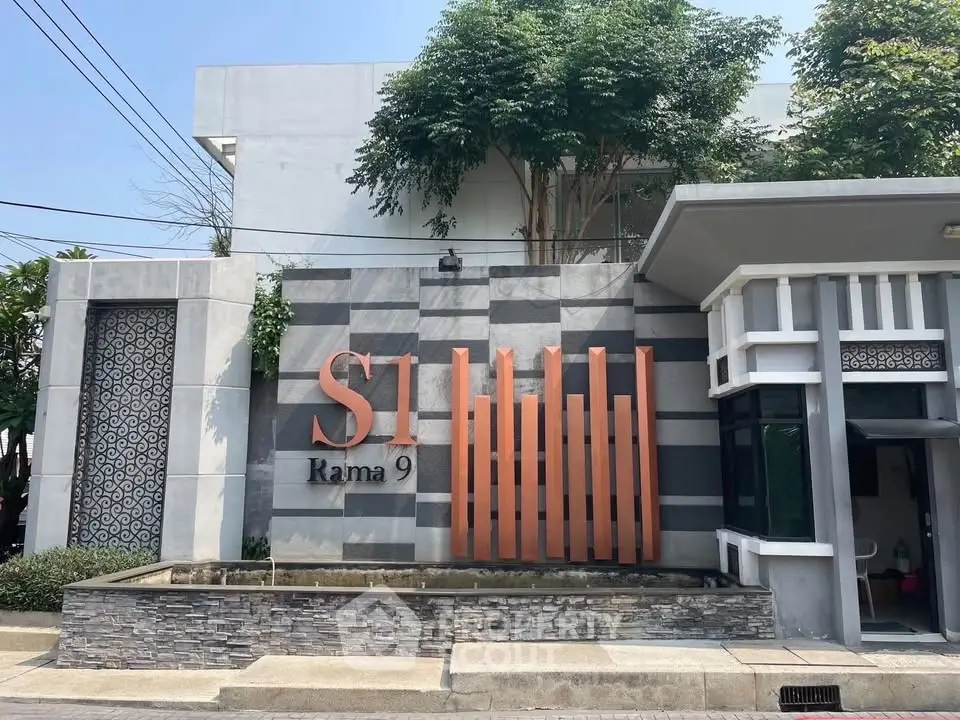Modern building entrance with stylish facade and signage at S1 Rama 9, showcasing contemporary architecture.