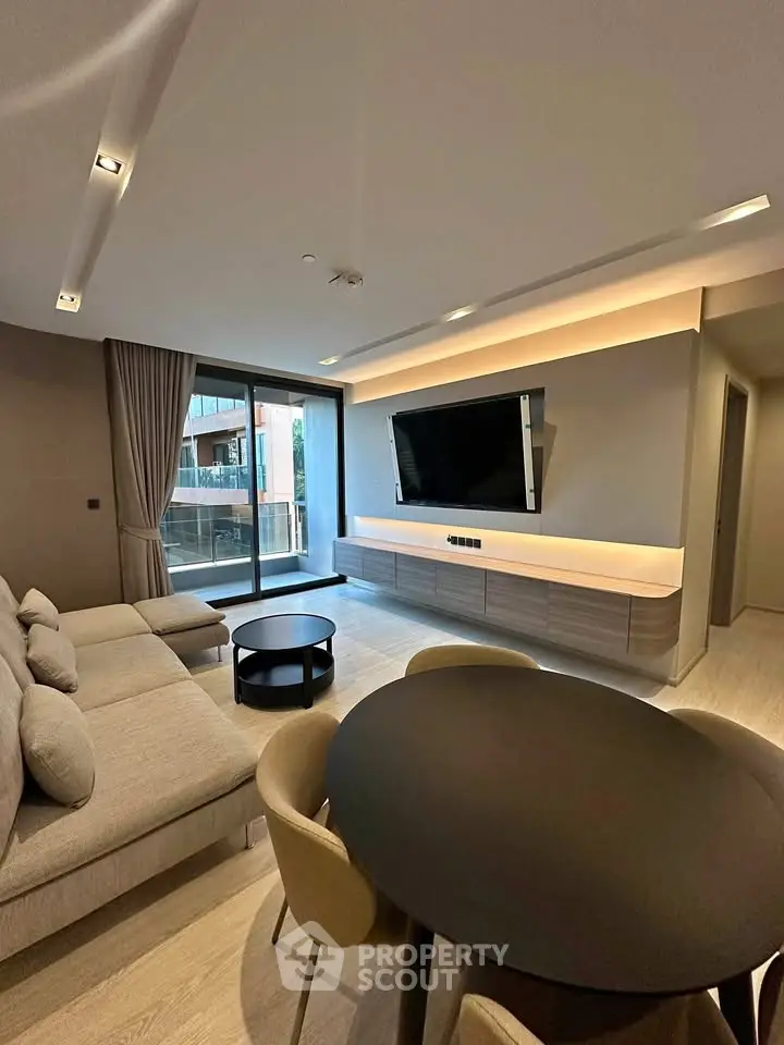 Modern living room with sleek furniture and large TV, featuring a spacious balcony view.