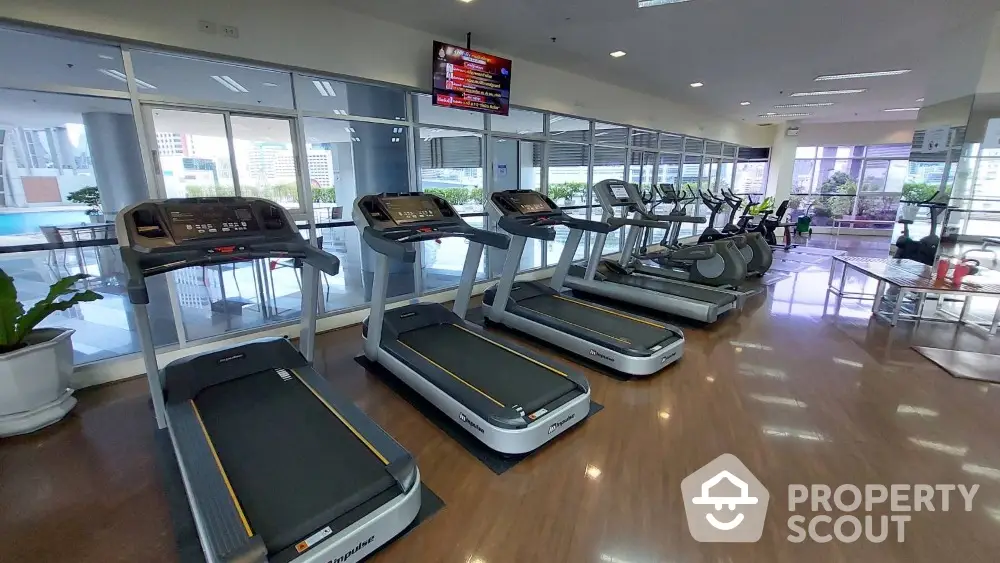 Spacious gym with modern equipment and city view, perfect for fitness enthusiasts.