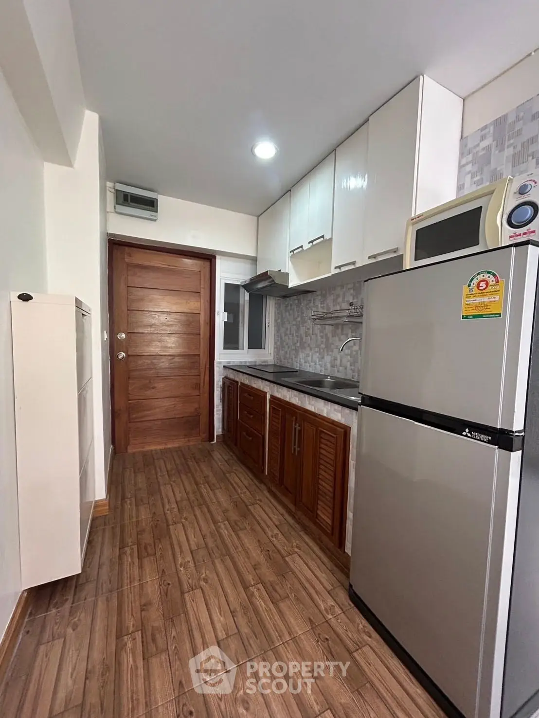 Modern kitchen with wooden cabinets, stainless steel fridge, and sleek countertops in a cozy apartment.