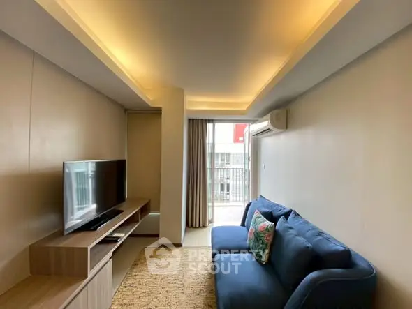 Modern living room with cozy blue sofa and flat-screen TV, featuring ambient ceiling lighting and balcony access.