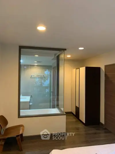 Modern bedroom with glass partition revealing a sleek bathroom and bathtub.
