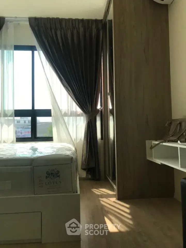 Bright bedroom with large window and elegant curtains, featuring a modern bed and wooden flooring.