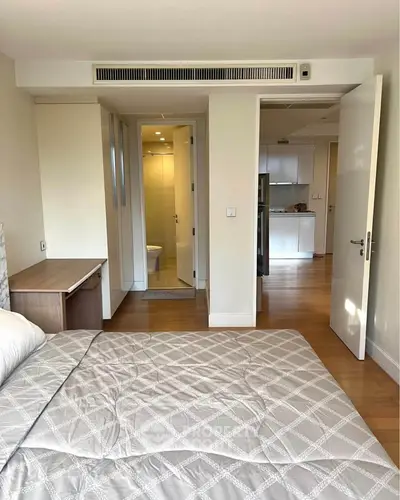 Modern bedroom with ensuite bathroom and view into kitchen area, featuring sleek design and wooden flooring.