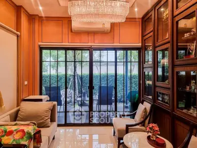 Luxurious living room with elegant chandelier and garden view through glass doors.