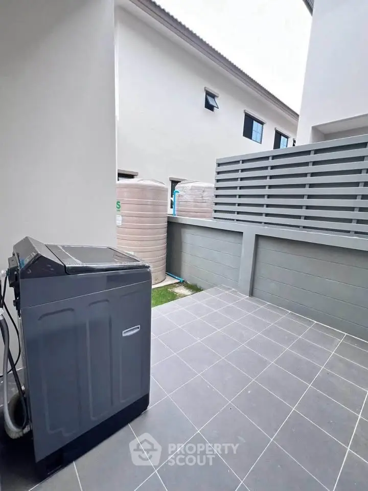 Modern outdoor laundry area with washing machine and water tanks in a stylish residential setting.