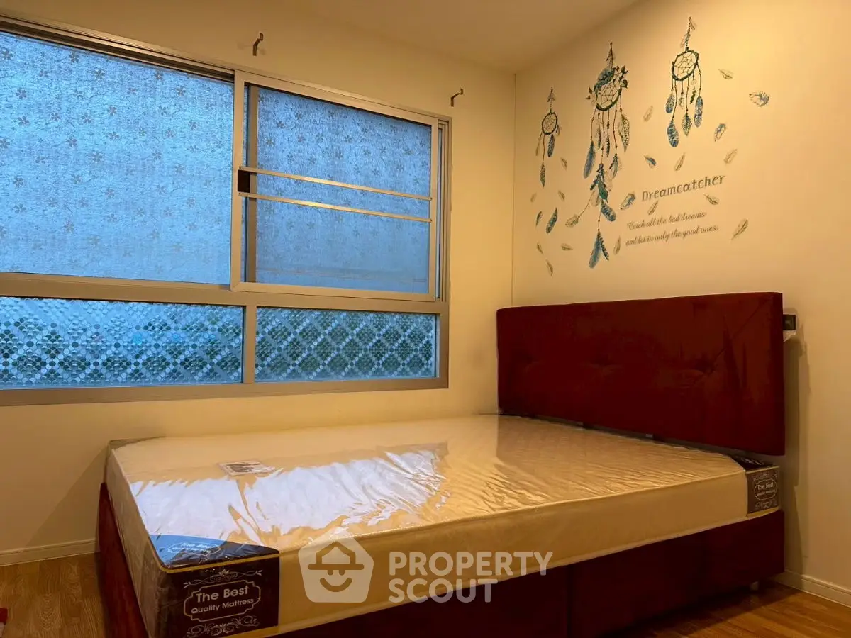 Cozy bedroom with dreamcatcher wall art and large window, perfect for relaxation.