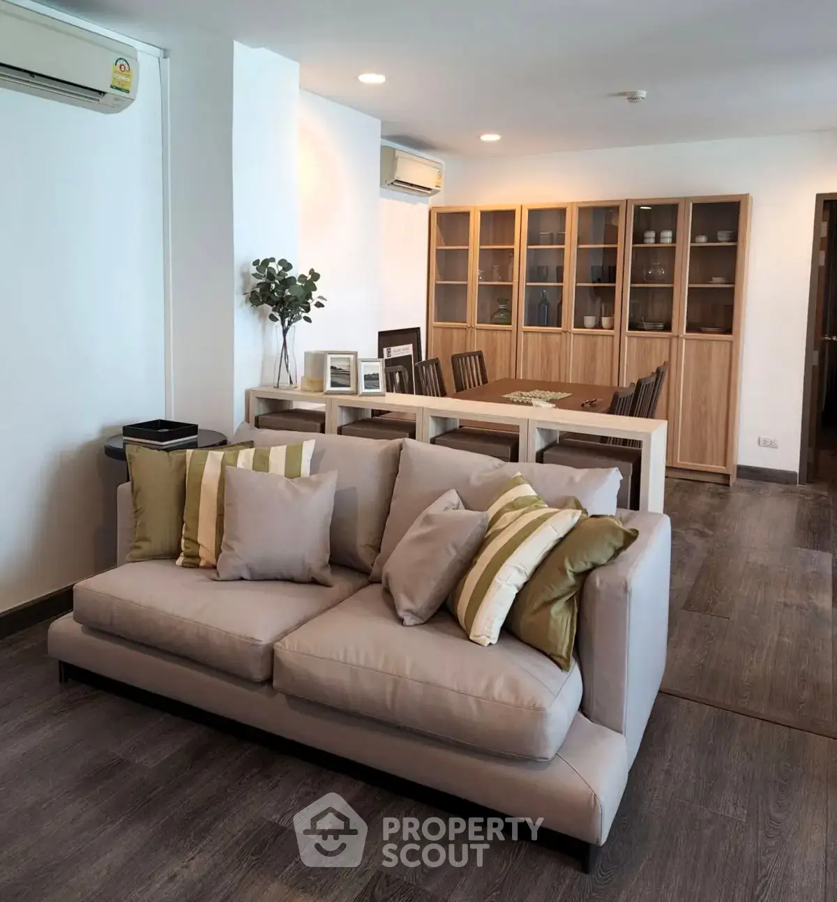 Spacious living room with modern decor and dining area, featuring elegant wooden flooring and stylish furniture.