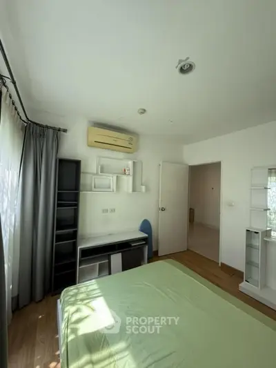 Bright bedroom with modern furnishings and air conditioning, featuring a large window and wooden flooring.