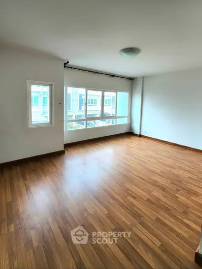 Spacious empty room with large windows and wooden flooring, perfect for customization.