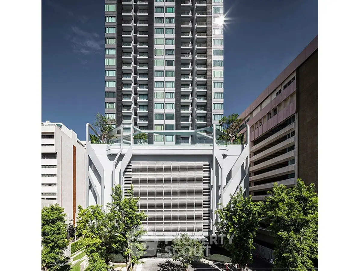 Modern high-rise building with sleek design and lush greenery in urban setting.