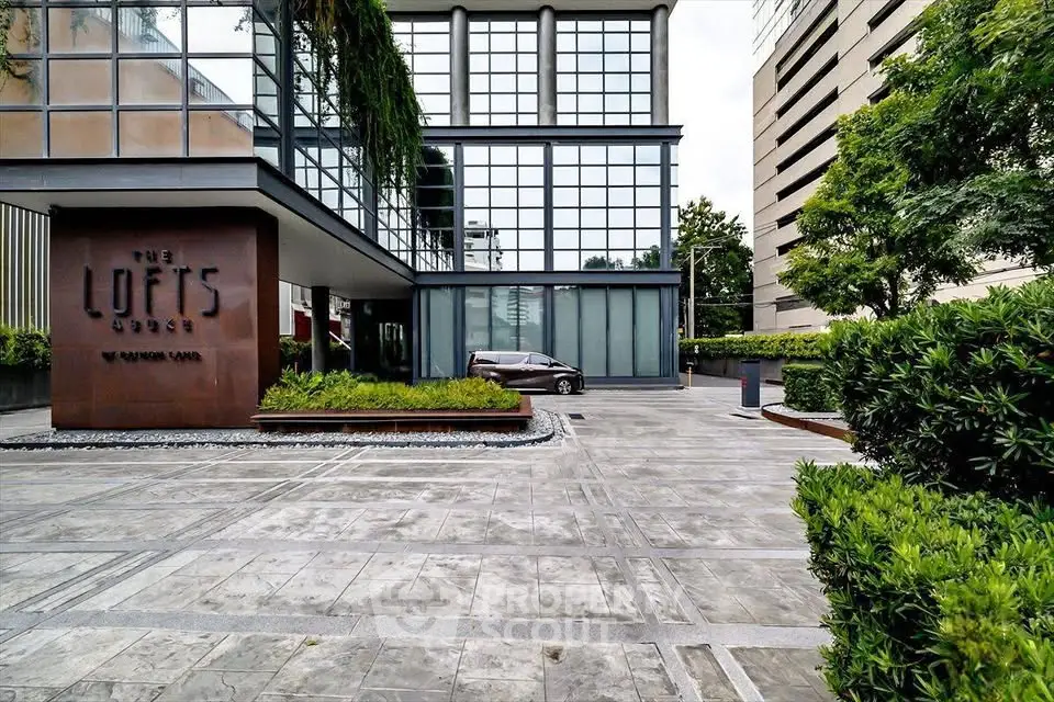 Modern building entrance with sleek design and lush greenery at The Lofts.