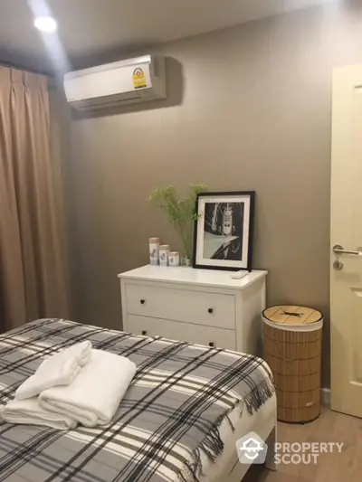 Cozy bedroom with modern decor and air conditioning, featuring a stylish dresser and framed artwork.