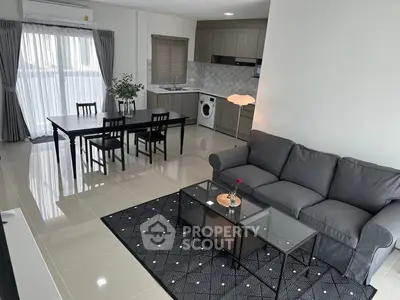Modern open-plan living room with sleek kitchen and dining area, featuring stylish furniture and natural light.