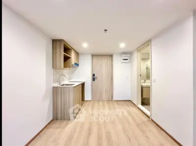 Modern minimalist apartment interior with compact kitchen and wooden flooring.