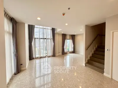 Spacious modern living room with large windows and elegant staircase in luxury apartment.