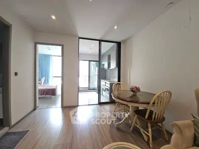 Modern apartment interior with open layout, featuring dining area and kitchen, leading to a bright bedroom.