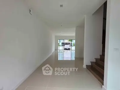 Spacious modern hallway with sleek tile flooring and staircase, leading to a bright entrance.
