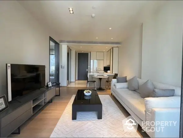 Spacious modern living room with plush seating, sleek entertainment unit, and abundant natural light, leading to an open-plan kitchen area.